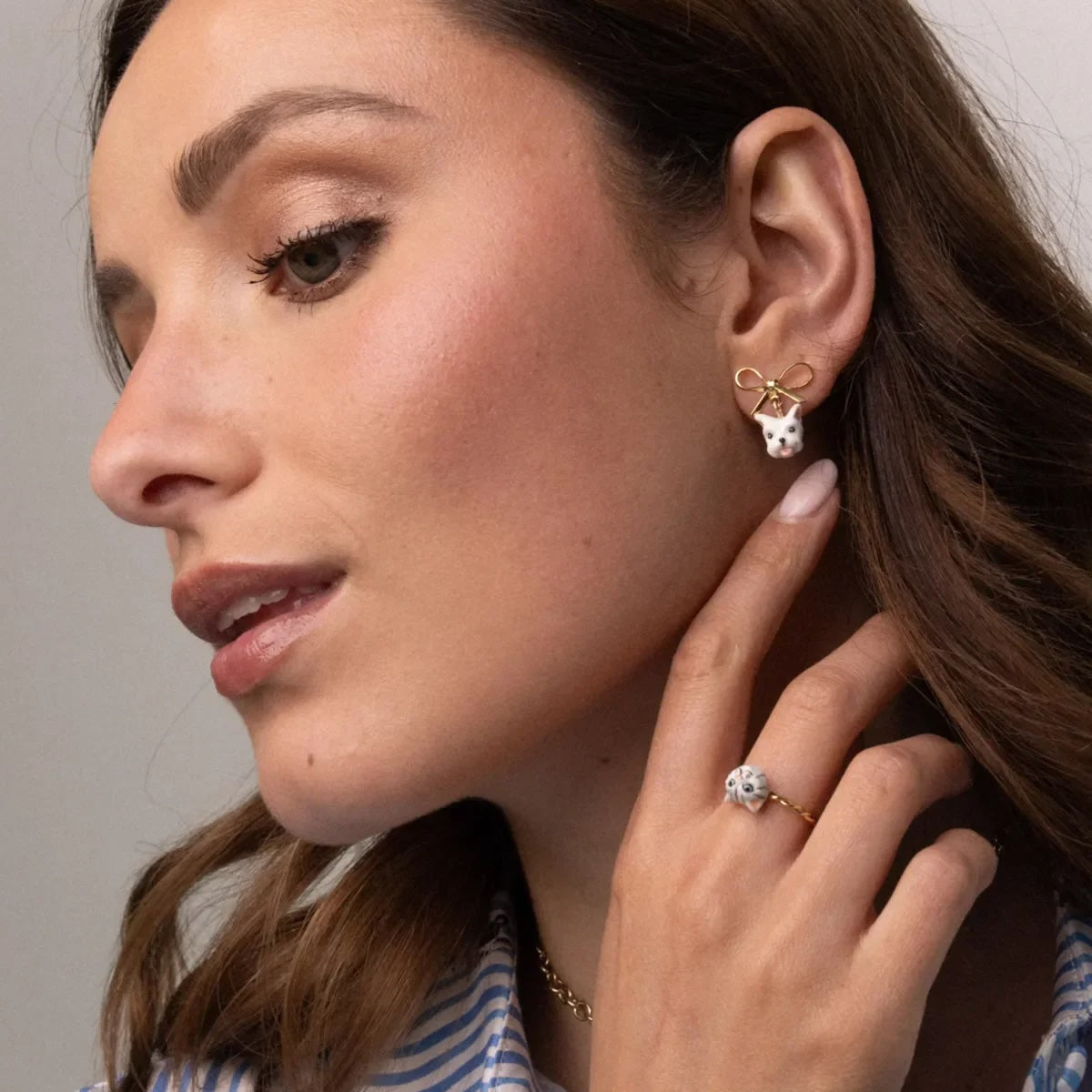 Close-up of a woman wearing earrings and a ring, with a neutral background