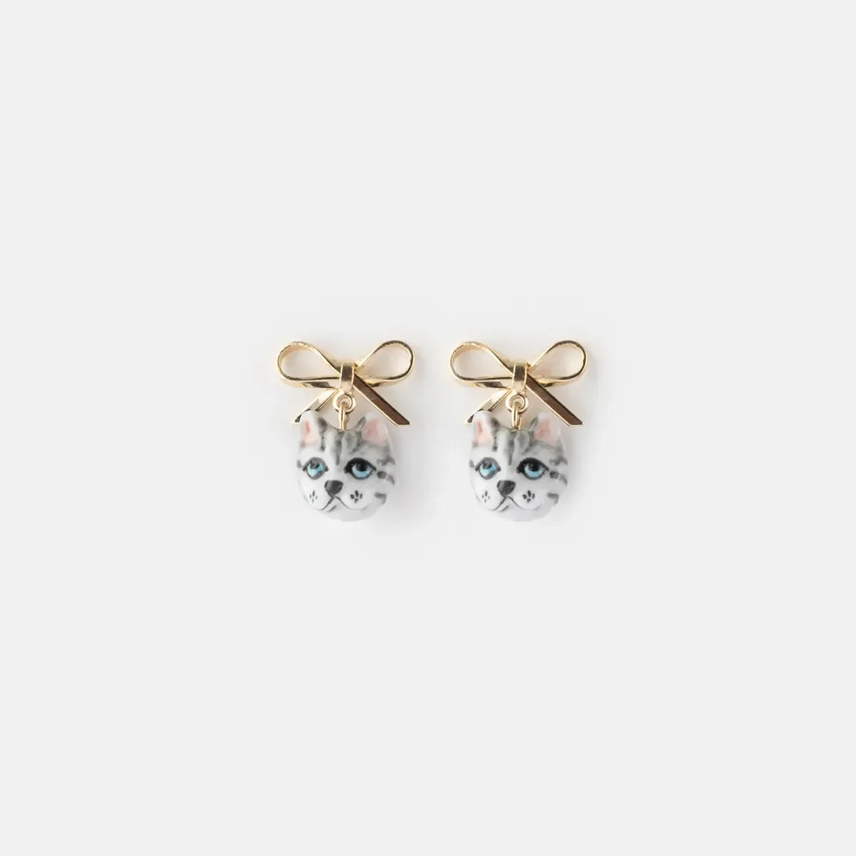 A pair of gold bow stud earrings with dangling cat face charms, shown on a plain light gray background.