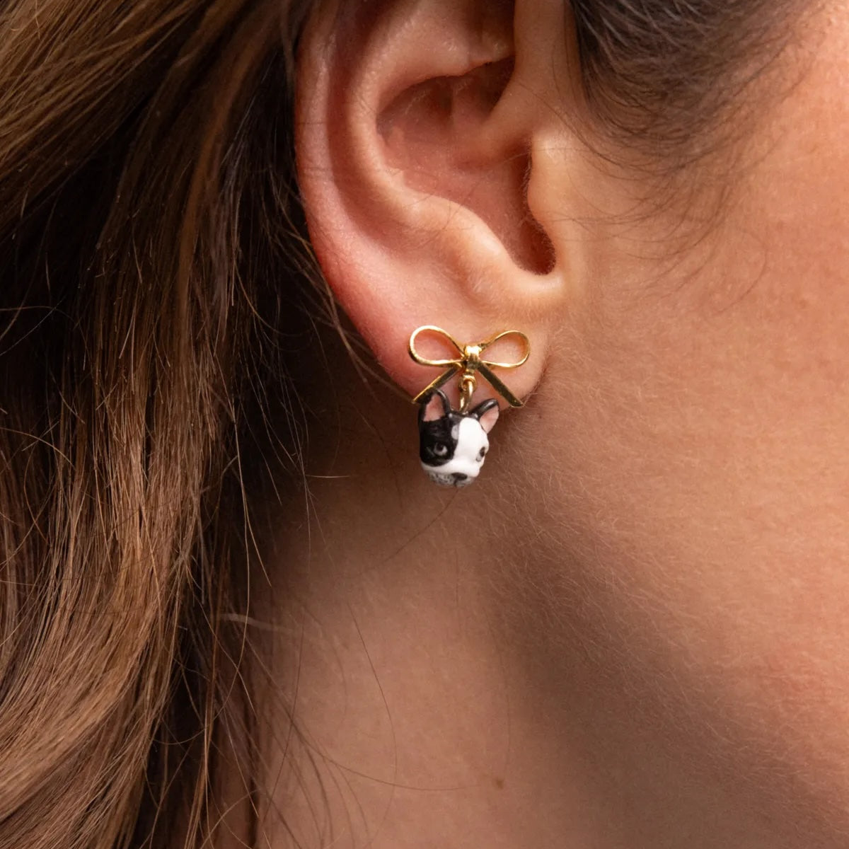 A close-up of a person's ear wearing a gold hoop earring with a bow and a small dangling black-and-white animal charm.