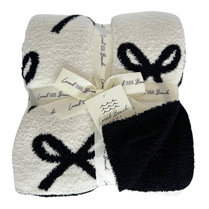 White blanket with black bow designs and a bow, branded 'Local Beach Home'.