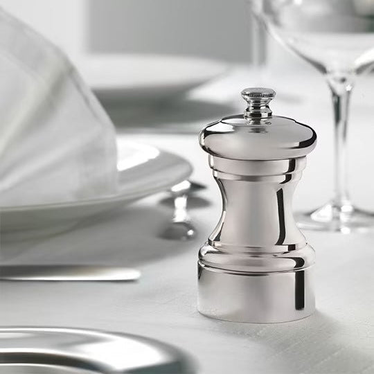 Silver pepper grinder on a table setting with white plates and glasses.