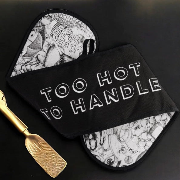 Black pot holder with 'Too Hot to Handle' text and gold spatula on a black background