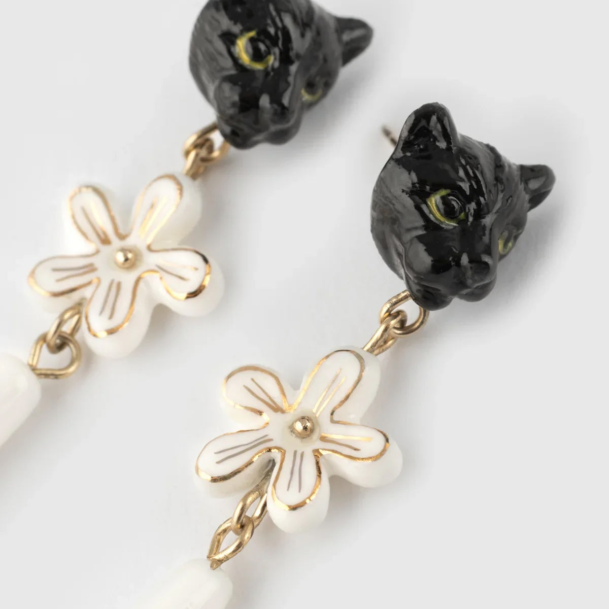 Black cat head drop earrings with white flower charms outlined in gold and white beads hanging below, shown on a light gray background.