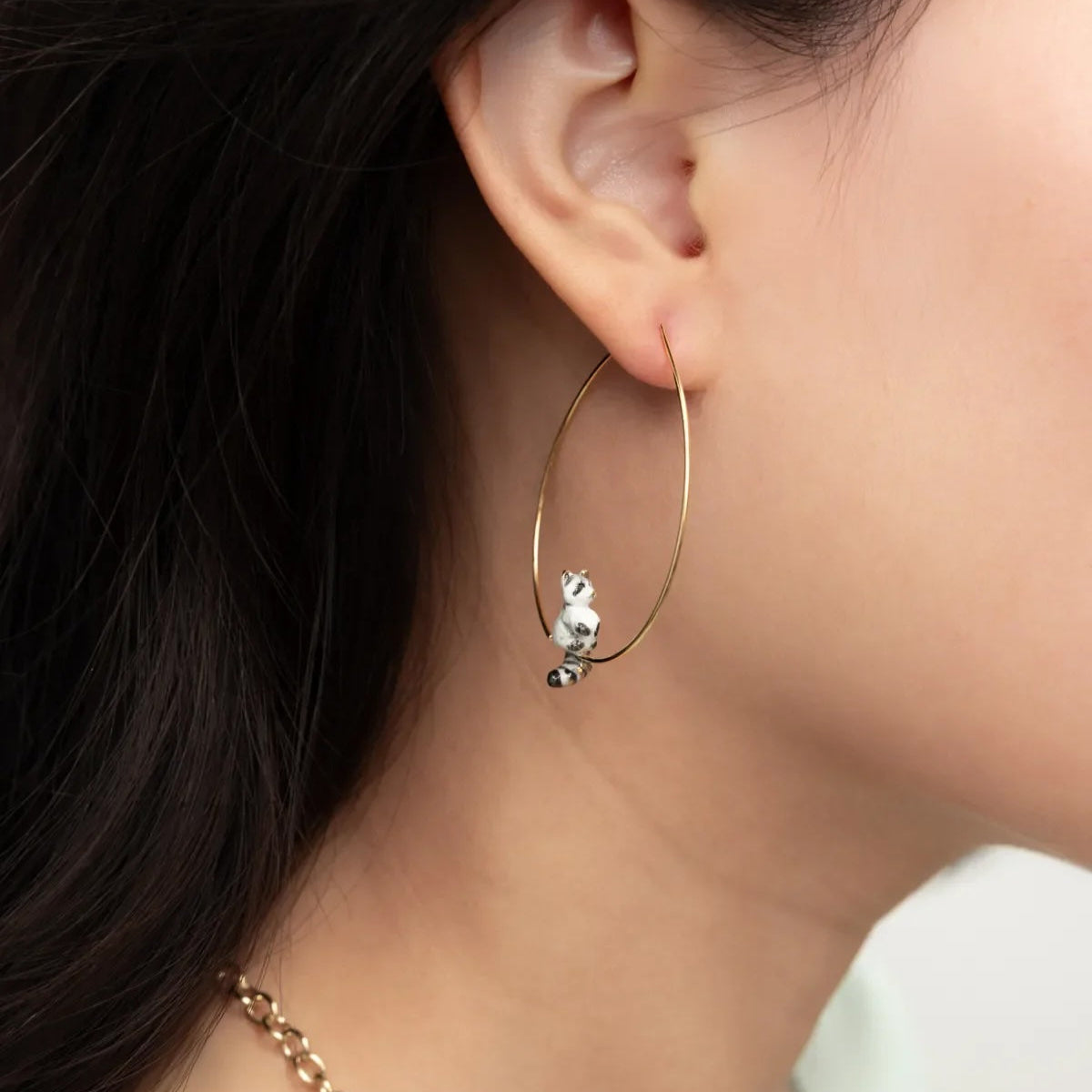 Gold hoop earring with a small animal charm worn by a person.
