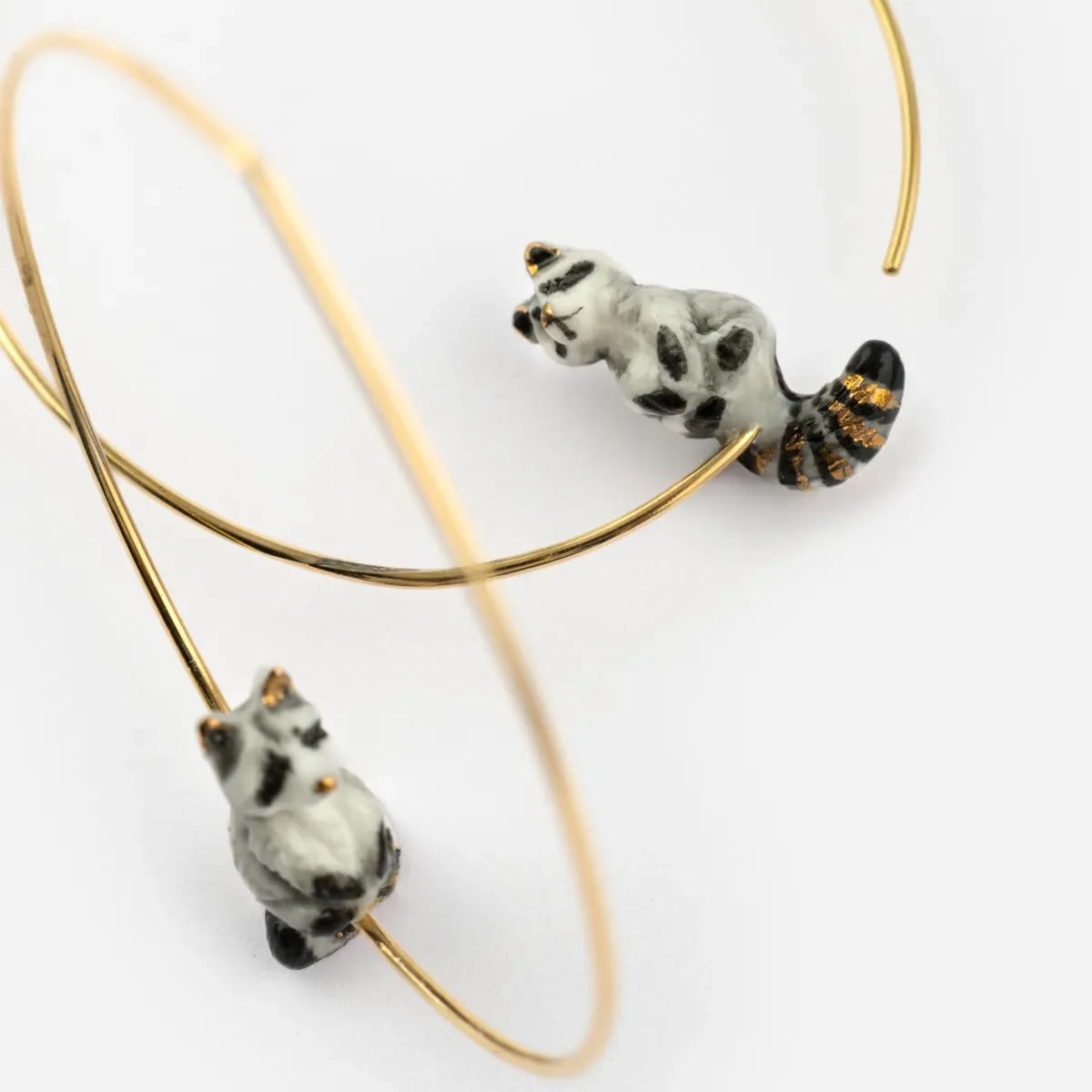 Gold hoop earrings with raccoon designs on a white background