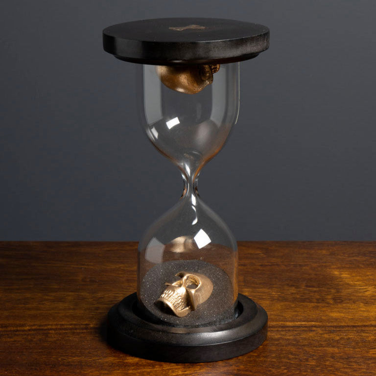 Hourglass with black top and base on a wooden surface against a dark background