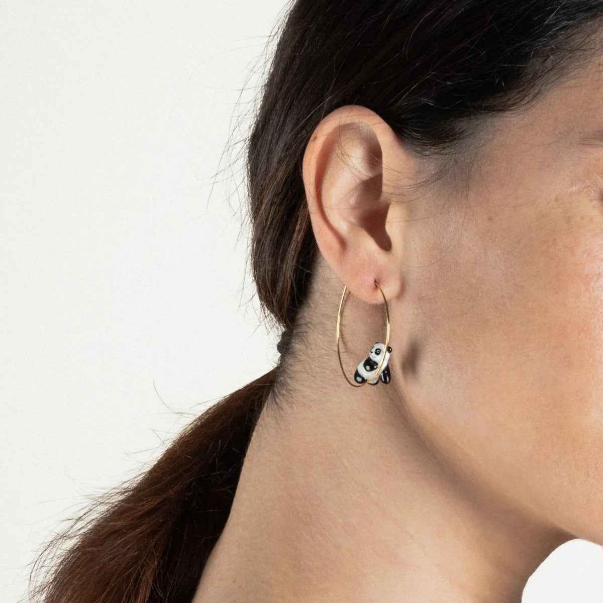 Close-up of a person wearing a small hoop earring with a panda design.