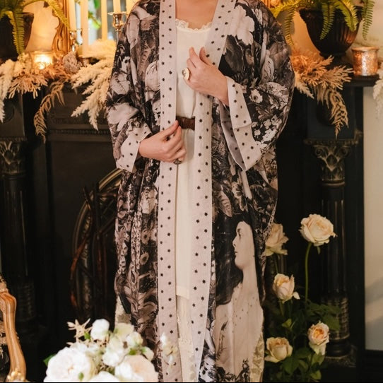 Woman in a patterned robe standing in a decorated room with candles and flowers.