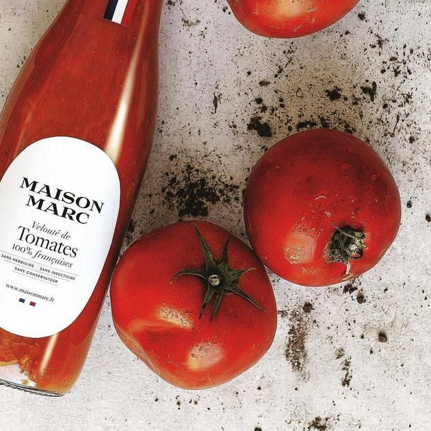Bottle of Maison Marc tomato paste with fresh tomatoes on a textured surface