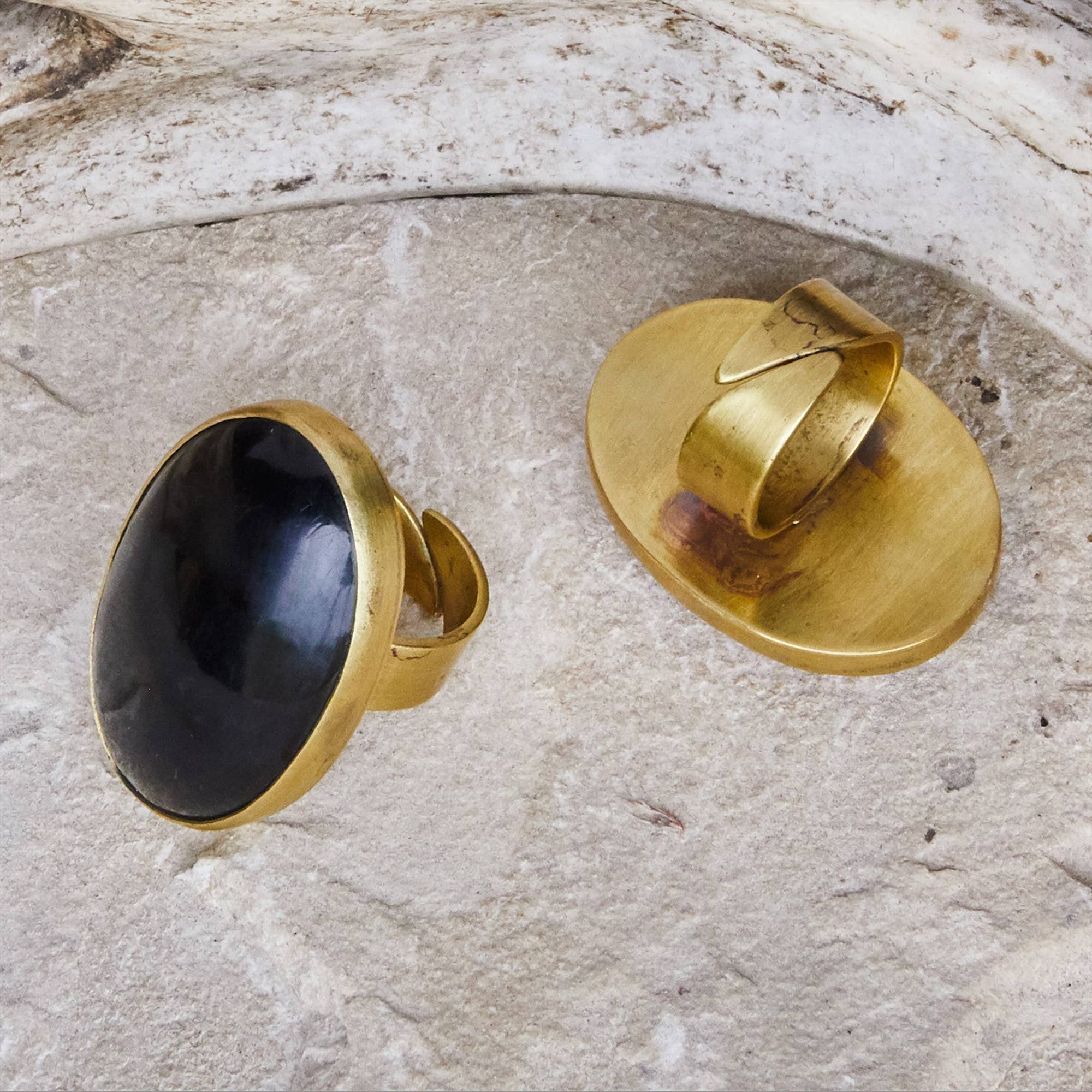 A gold ring with a large oval black stone, shown from both front and back on a textured light gray stone surface.