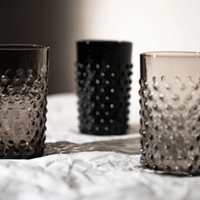 Three textured glass tumblers on a textured surface with a blurred background