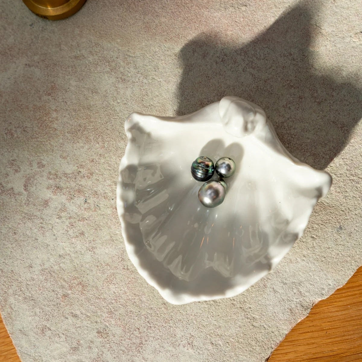 Shell-shaped dish with jewelry on a textured surface next to a candle