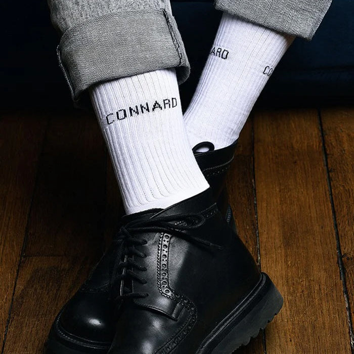 Black leather boots worn with white socks on a wooden floor