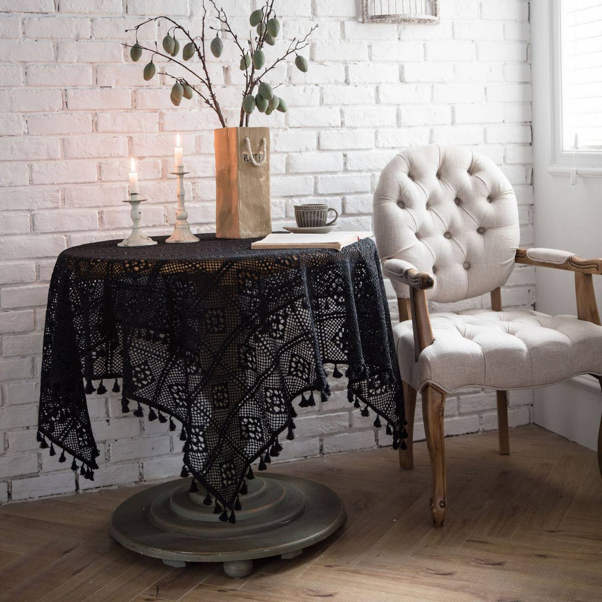 Black crochet lace tablecloth with tassel edging draped over a round table by a white brick wall – ACCITY