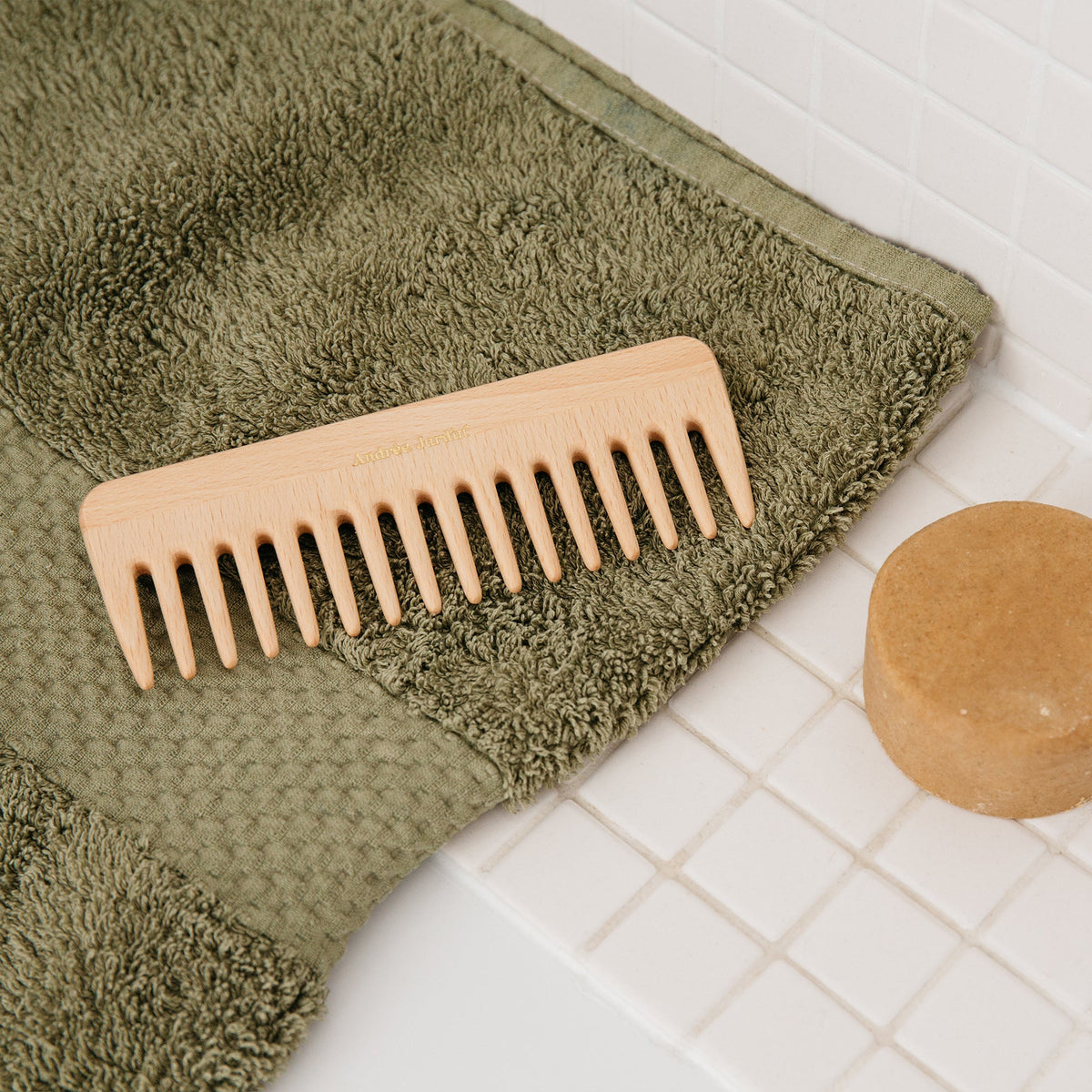 Wide-tooth beech comb on a sage green towel beside a round bar of soap – Andrée Jardin