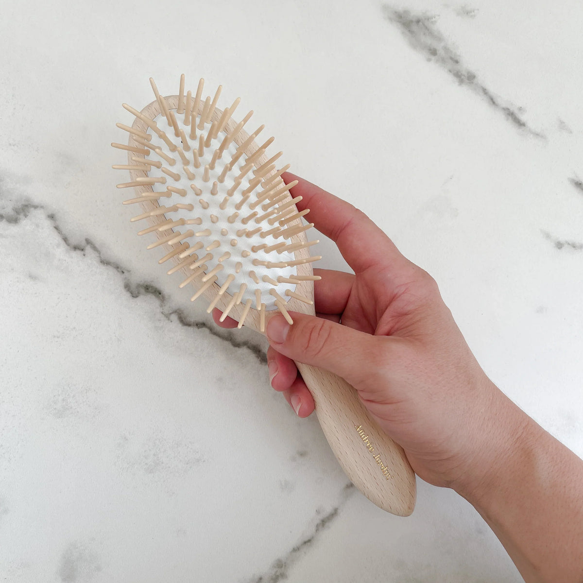 Close-up of a hand holding the brush, showing the rounded wooden pins set in the rubber cushion – Andrée Jardin