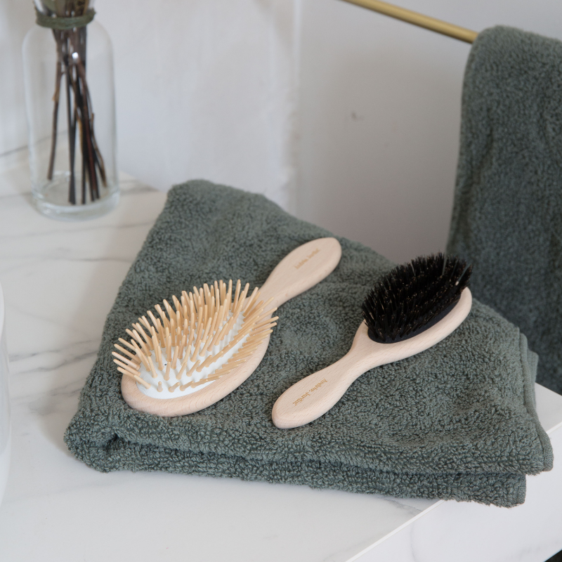 Wooden-pin detangling brushes in both sizes on a folded sage green towel, beside a boar bristle brush – Andrée Jardin