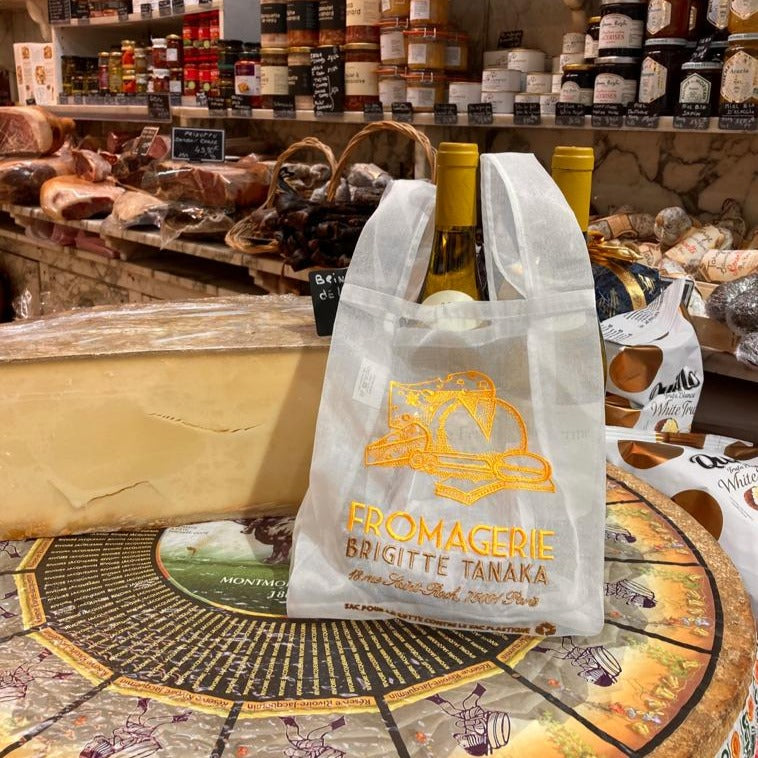 Fromagerie organza bag holding a wine bottle in front of a cheese counter – Brigitte Tanaka