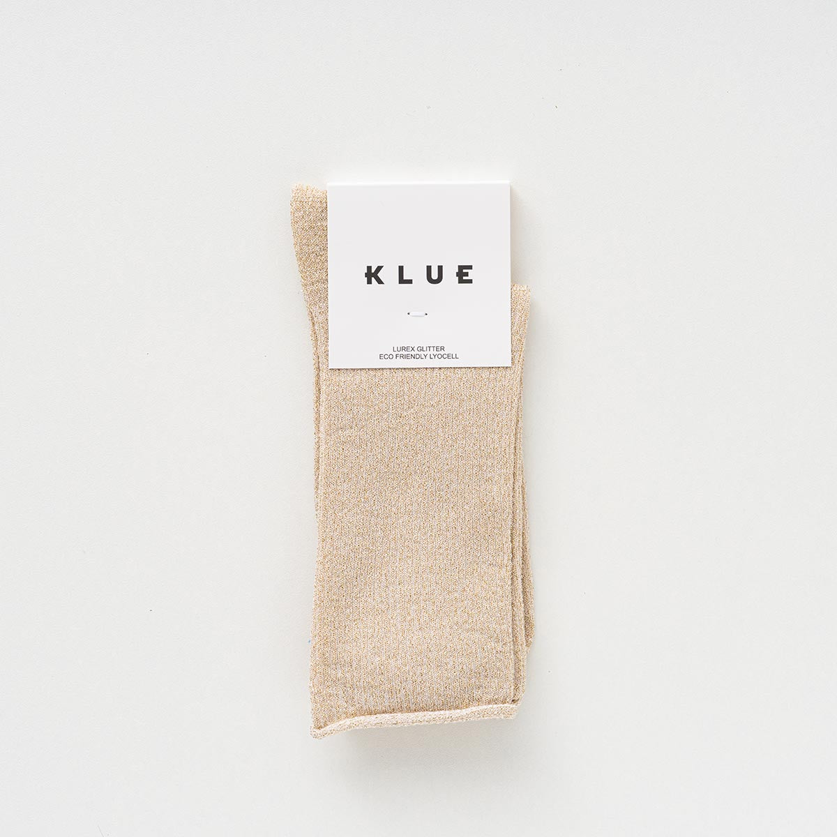 Folded pair of pale beige socks with a golden lurex shimmer in a KLUE paper band – KLUE