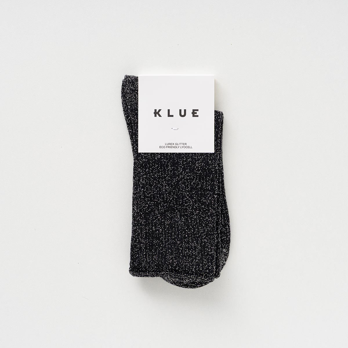 Folded pair of black socks with a silver lurex shimmer in a KLUE paper band – KLUE