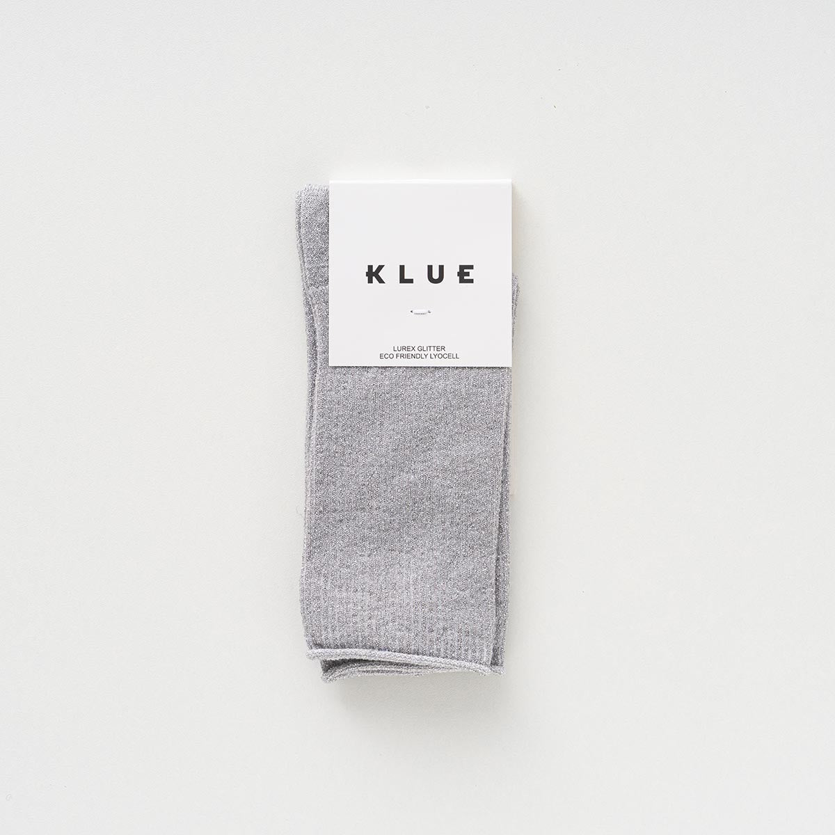 Folded pair of light silver-grey socks with a soft glitter in a KLUE paper band – KLUE