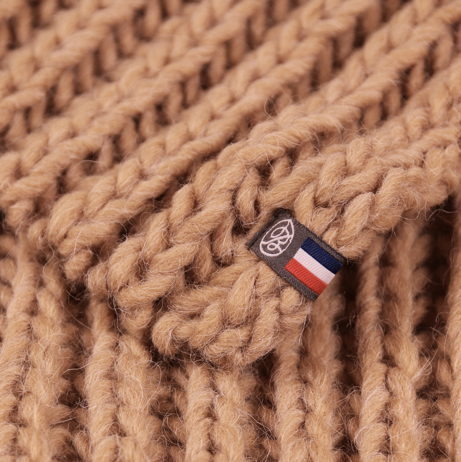 Close-up of a beige knitted fabric with a brand label featuring red, white, and blue stripes.