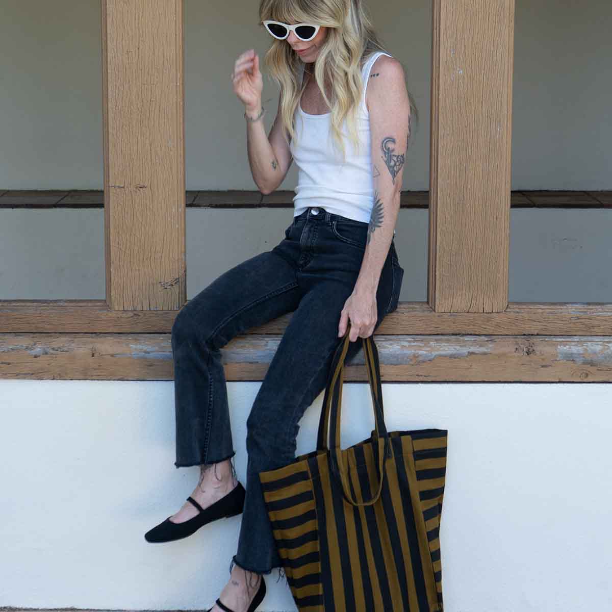 Woman in black jeans holding the striped cumin tote by its handles outdoors – Rose in April