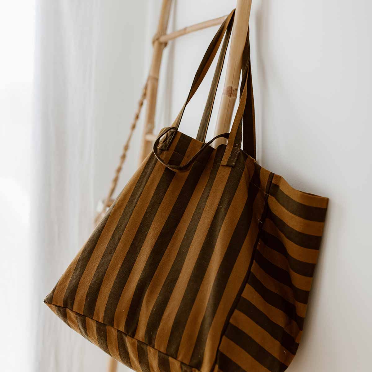 Striped cumin canvas tote hanging from a wooden ladder, showing its two handle lengths – Rose in April