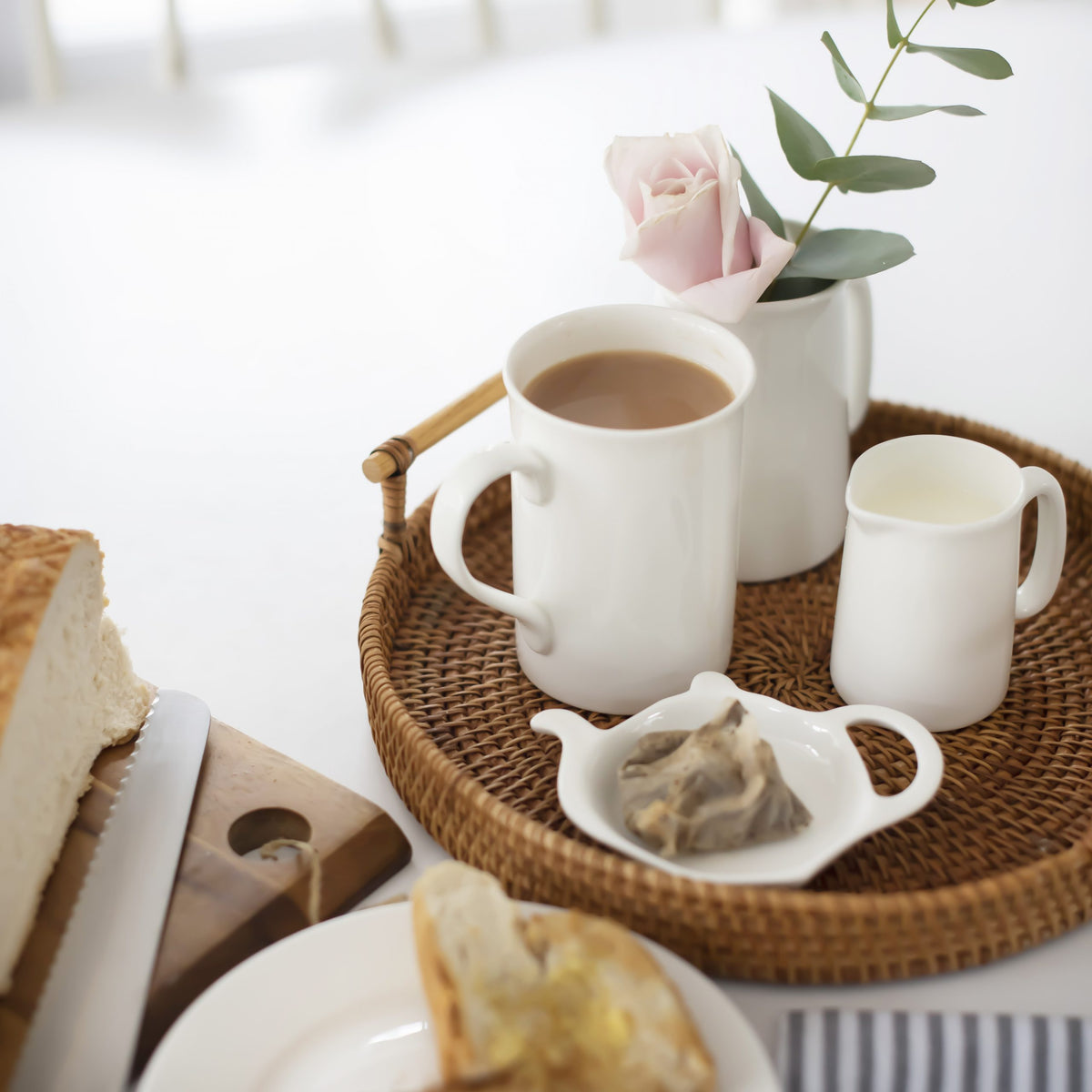 Teapot-shaped white teabag rest on a rattan tray with a mug and milk jug – Buttercup