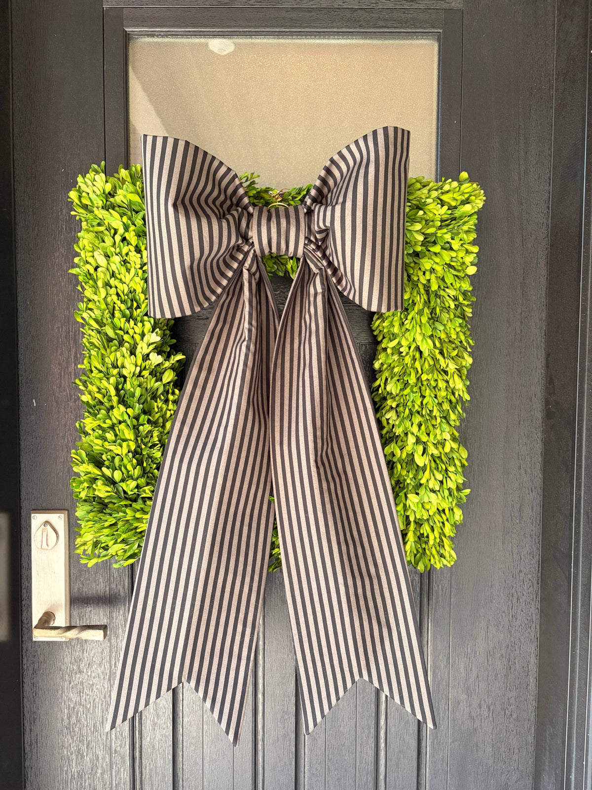 Charcoal and ivory striped bow over a boxwood wreath on a dark front door – La Maison Reverie